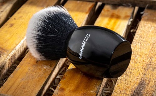 En rund svart behållare med en vit- och svart makeupborste på en träyta.