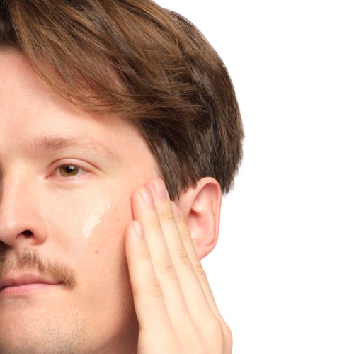 A person touching their face near the cheek, with brown hair and light skin. The image is a close-up.