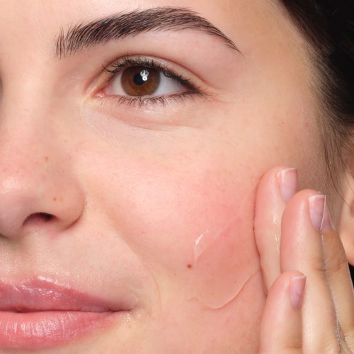 Nahaufnahme einer Frau, die ihre Wange berührt, mit klarer Haut und natürlichem Make-up.