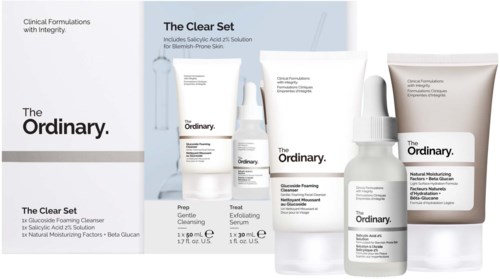 A skincare set including cleanser, exfoliant, serum, foaming solution, and moisturizer in white bottles and tubes.