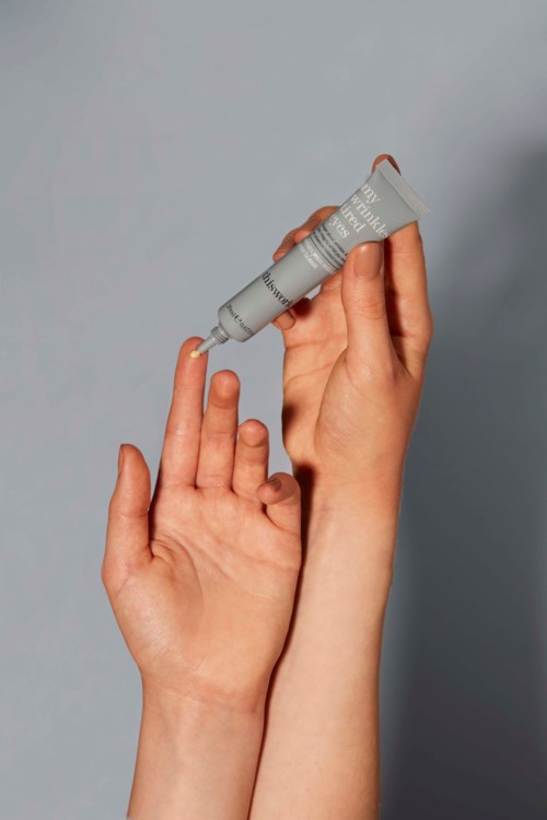 En person påfører creme eller maling på sit finger med en tube, mod en neutral baggrund.