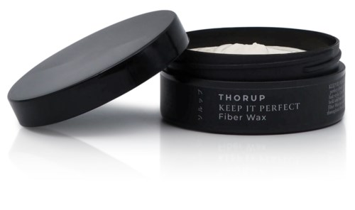 En svart behållare med lock märkt 'Thorup Keep It Perfect Fiber Wax' som innehåller vax. Locket är delvis öppet.