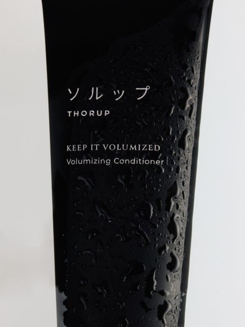 Svart flaske med japanske tegn, hvite ord "THORUP" og beskrivelse av volumgivende balsam.