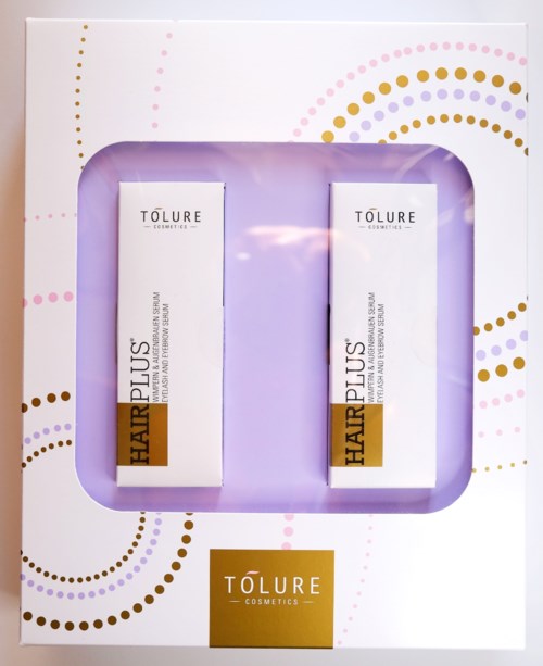 Kaksi Tolure Cosmetics Hair Plus -rasvahappopakettia ovat sisällä koristeellisessa violetissa ja valkoisessa laatikossa, jossa on värikkäitä täplikkäitä kuvioita.