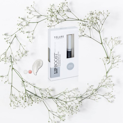 En hudpleiepakke merket 'LIP BOOST' omgitt av tynne hvite blomster på hvit bakgrunn.