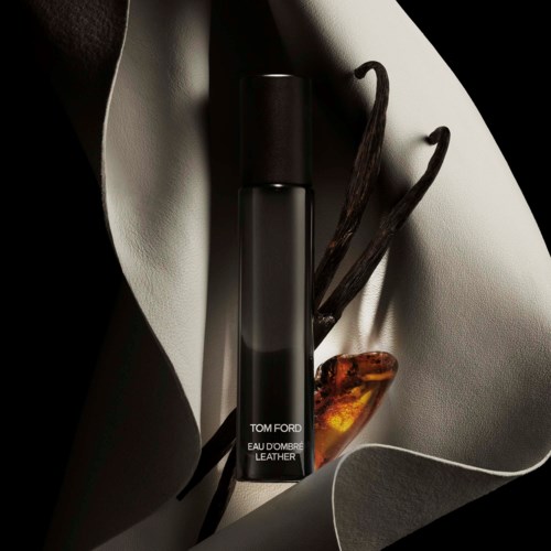 A Tom Ford perfume bottle surrounded by vanilla pods, amber stone, and white fabric with shadows.