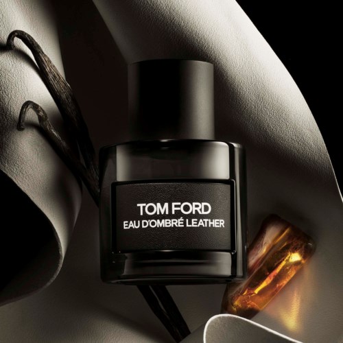 Black Tom Ford perfume bottle with white text and a gold-colored object nearby in a stylish setting.