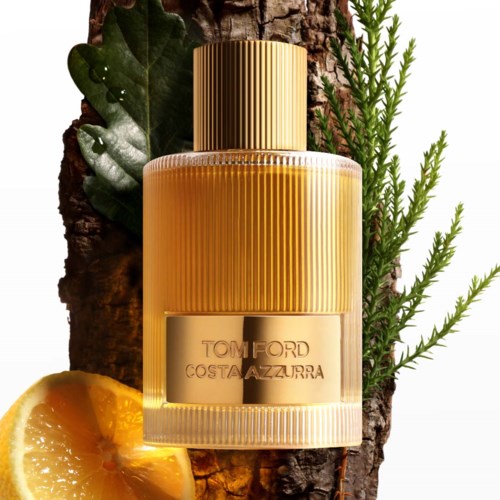 A perfume bottle named Tom Ford Costa Azzurra, placed on a tree trunk with leaves and an orange slice nearby.