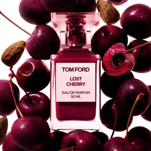 A pink perfume bottle labeled "Lost Cherry" surrounded by fresh cherries and cherries with pits and stems.