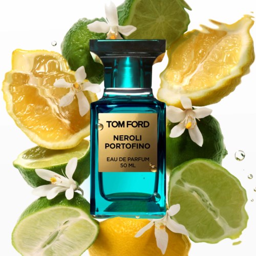 En parfymflaska omgiven av skivade citroner, lime och vita blommor, med lite juice och vattendroppar.