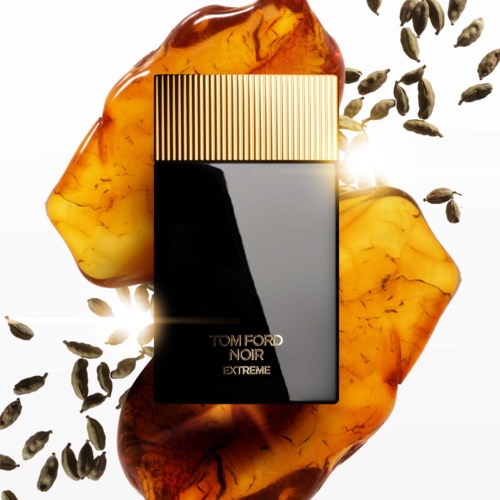 En svart parfymflaska märkt "Tom Ford Noir Extreme" omgiven av bärnstenfärgade stenar och utspridda svarta frön.