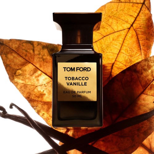 A black perfume bottle labeled 'Tom Ford Tobacco Vanille' sits among fall leaves.
