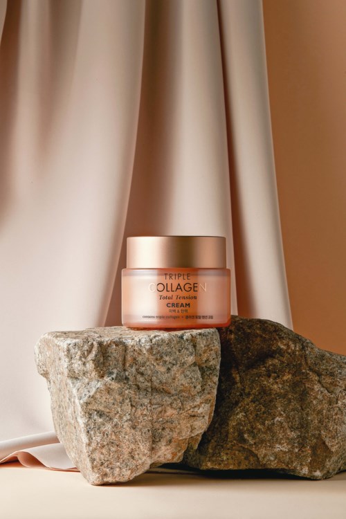 A jar of cream placed on two rocks with beige and brown background curtains.