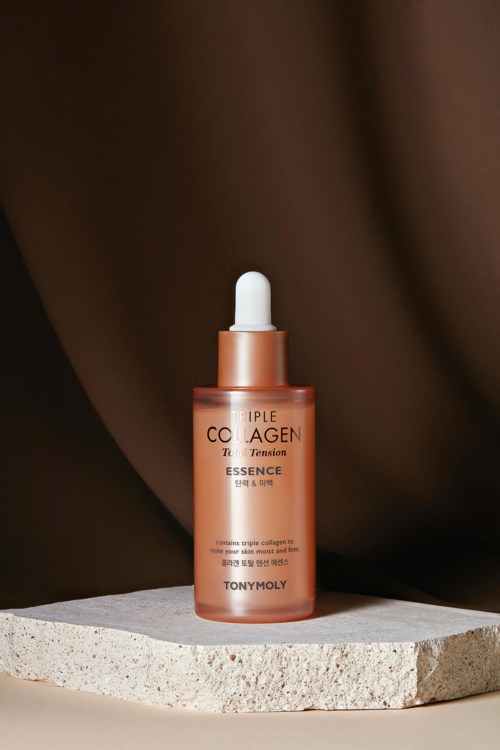 A small, copper-colored bottle with a dropper sits on a concrete surface, against a brown fabric background.