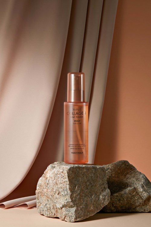 A bottle of skincare product on rocks with a soft background curtain, warm lighting, and minimal decor.