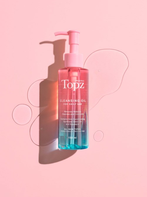 En pink og blå renseolieflaske med pumpe på en pink baggrund, med nogle flydende cirkler i nærheden.