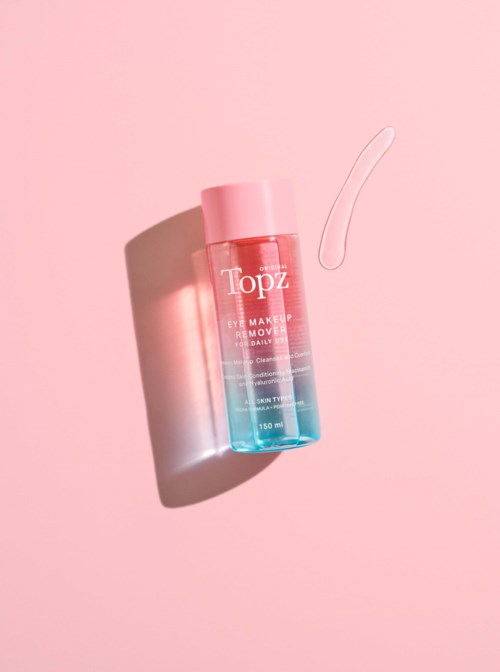 En rosa och blå flaska med make-up remover och en liten kladd bredvid på en rosa bakgrund.