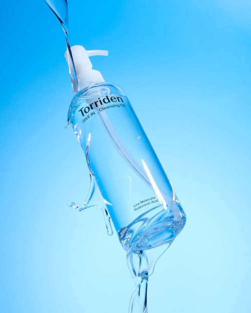 Eine klare Flasche mit Reinigungsöl und Pumpen, geneigt mit Wasser spritzend vor blauem Hintergrund.