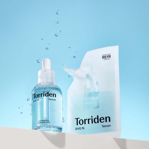 Een heldere fles Torriden Dive In serum met pipet en een refillverpakking op een witte rand tegen een blauwe achtergrond.
