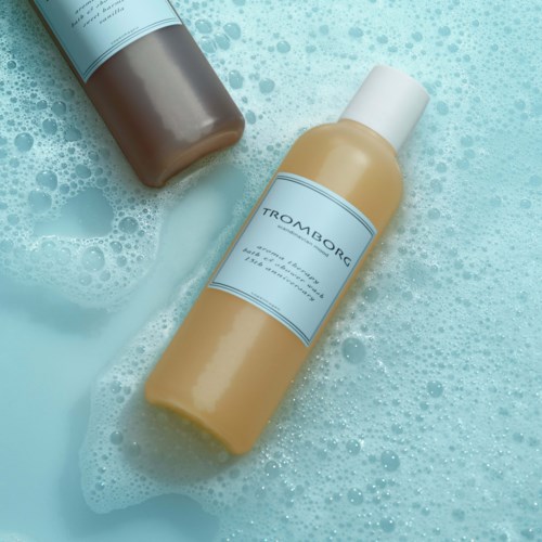 To flasker med shampoo eller badedrik i et skummende, blåt miljø. Den ene er beige, den anden er brun.
