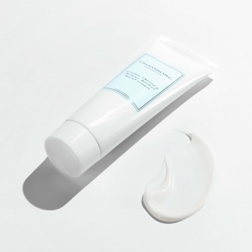 Vit tub med kräm eller lotion, med lite av produkten utpumpad bredvid på en vit bakgrund.