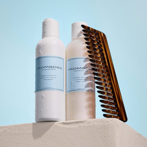 Två vita flaskor med blå etiketter och en brun kam vilar på en yta mot en blå bakgrund.