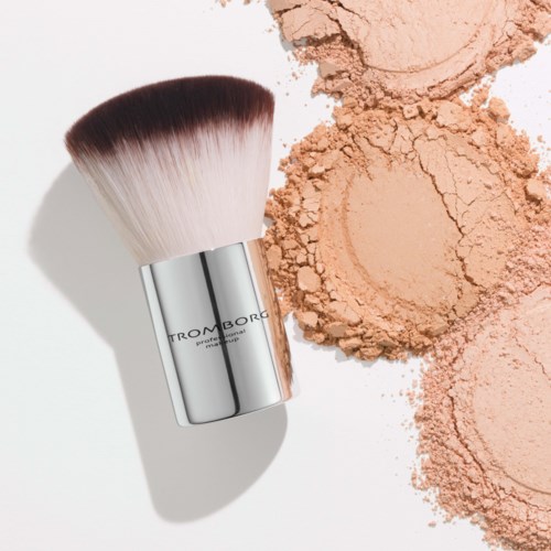 En makeup-børste med pulver spredt ud ved siden af på en hvid overflade.