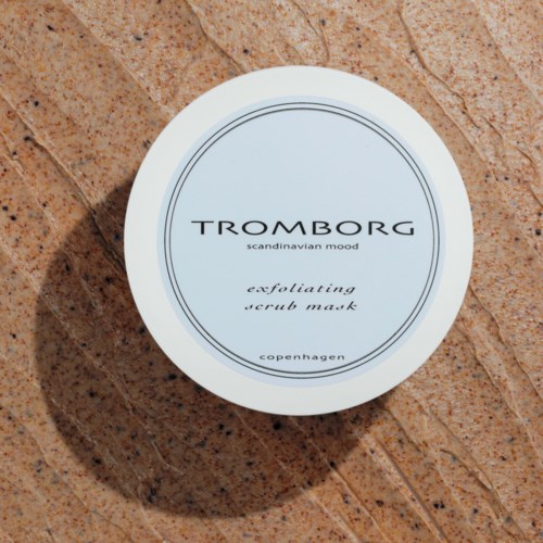 En hvid beholder med eksfolierende scrubmaske på tekstureret brun overflade, mærket 'TROMBORG' med 'scandinavian mood' og 'copenhagen'.