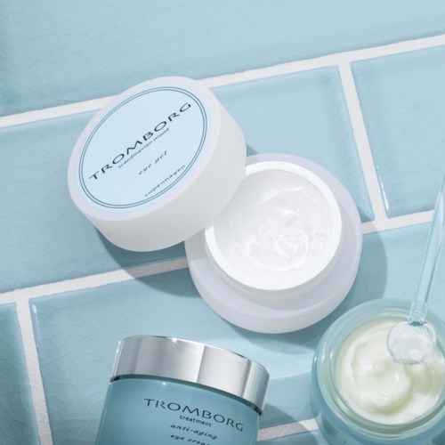 Hudplejeprodukter, herunder creme i krukke og behandling i tube, vises på en fliseoverflade.