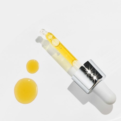 Een pipet met gele vloeistof, twee gele pillen en een witte achtergrond.