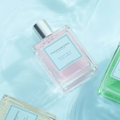Tre parfume-flasker på en lys blå overflade med forskellige pastel-farvede væsker indeni.