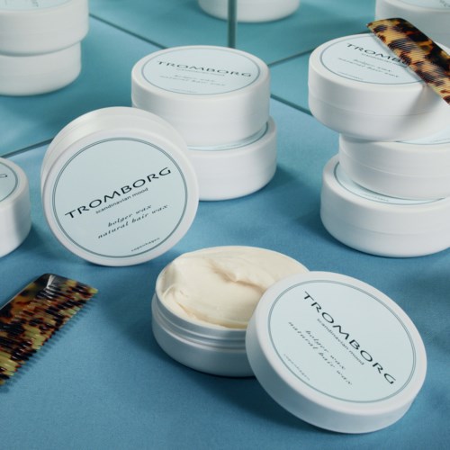 Ronde witte potjes met 'TROMBORG' label, gevuld met crème, op een blauwe ondergrond met spiegelreflexie.