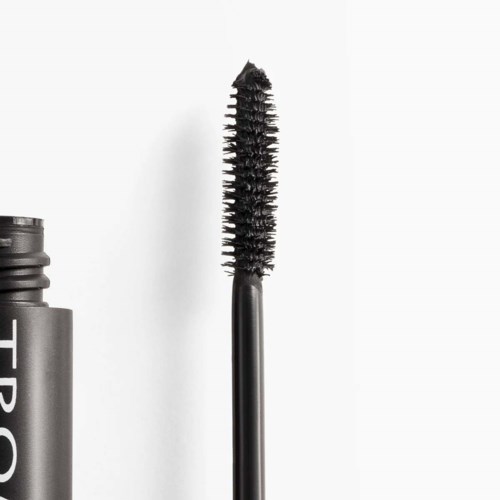 En sort mascara-børste med en pigget børste over en grå beholder med hvid skrift.