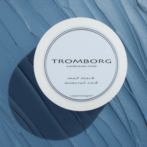 En hvid rund beholder på en tekstureret blå overflade. Etiketten siger 'Tromborg Scandinavian Mood Mud Mask'.