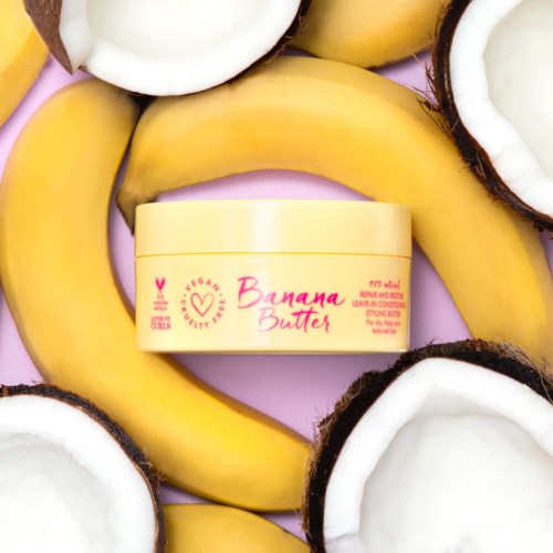 En burk banansmörgås omgiven av bananer och kokosnötter på rosa bakgrund.