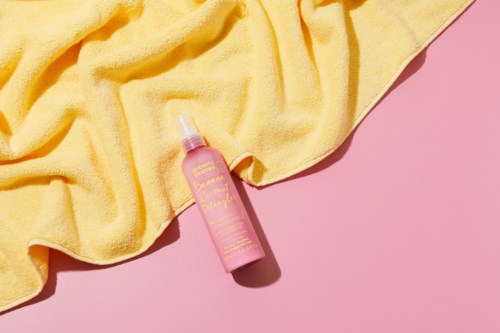 Rosa sprayflaska med gul handduk på rosa bakgrund.
