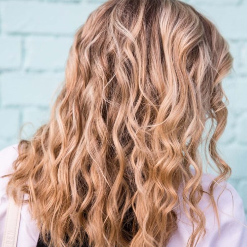 Wavy blonde hair flows over a person's back against a light blue background.