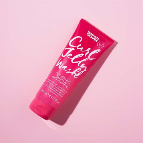 En rosa tub med krääm för lockigt hår med vitamin B5, märkt som Carol Jelly Wash, ligger på en rosa bakgrund.