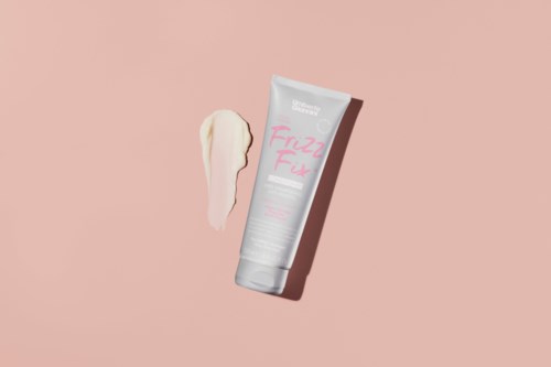 This is a tube of cream with a dollop of it on a pink background.
