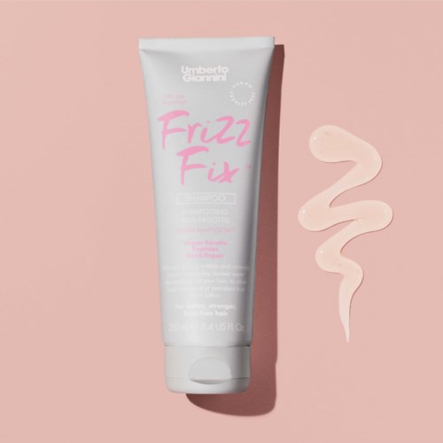 White tube of hair product with pink and gray text, placed on pink background with cream-colored swirl.