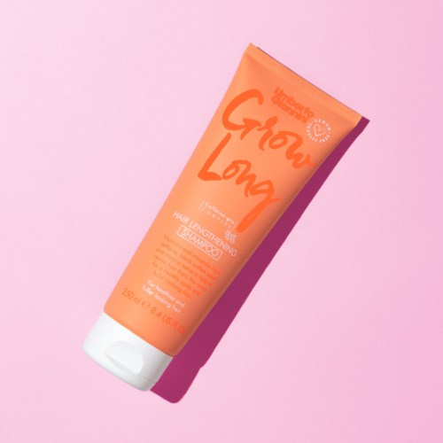 En persikfärgad tub med helstärkande serum för hår, med orange text och vit kork, placerad på en rosa bakgrund.