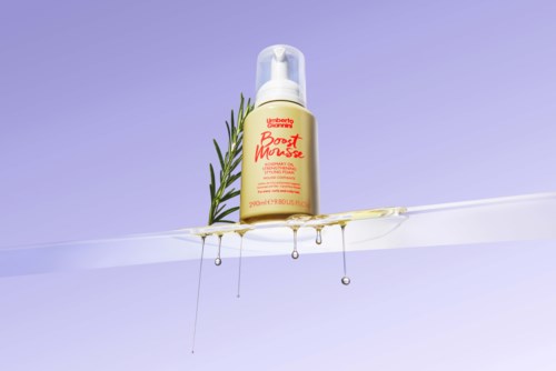 En gul flaska märkt 'Beauty Boost Mousse' med en timjankvist och honung som rinner från den på en tydlig yta.
