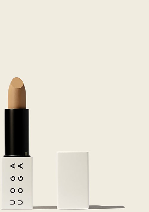 En beige læbestift med sort og hvid emballage, står oprejst ved siden af en hvid hat. Enkel og minimalistisk design.