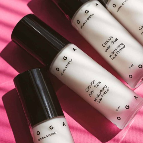 Three white bottles with black caps lie on pink fabric, labeled as face primer, moisturizing and organic.
