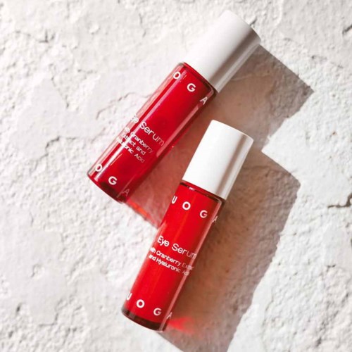 Two red bottles labeled 'Eye Serum' are placed on a white textured surface, casting shadows.