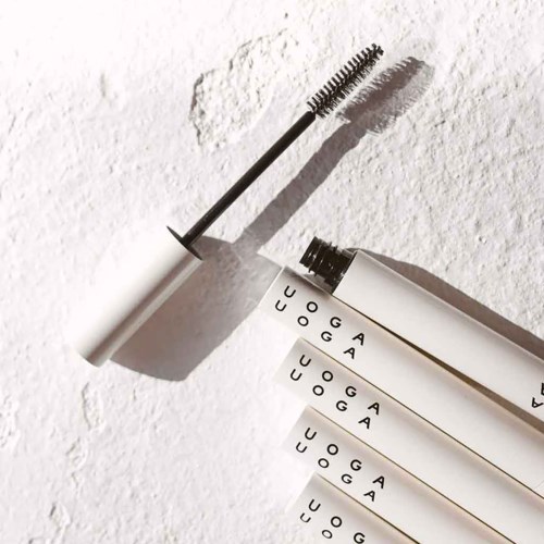 A mascara wand with a black and white tube, casting shadows on a textured white surface.