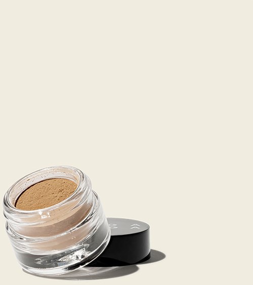 En liten burk med brunt pulver makeup, med ett svart lock bredvid på en ljus bakgrund.