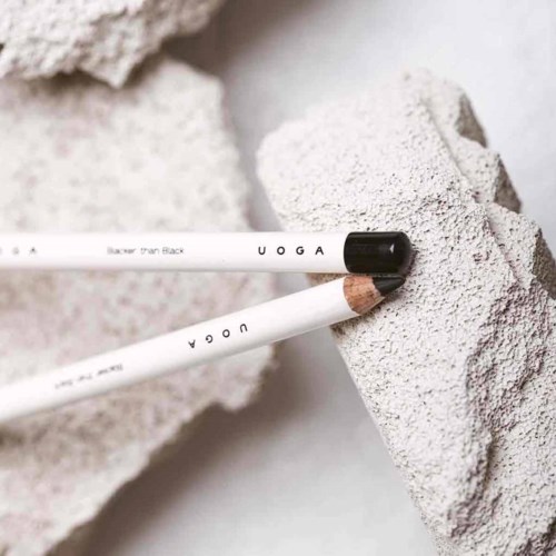 Two white makeup brushes with black and brown tips resting on textured gray rocks.