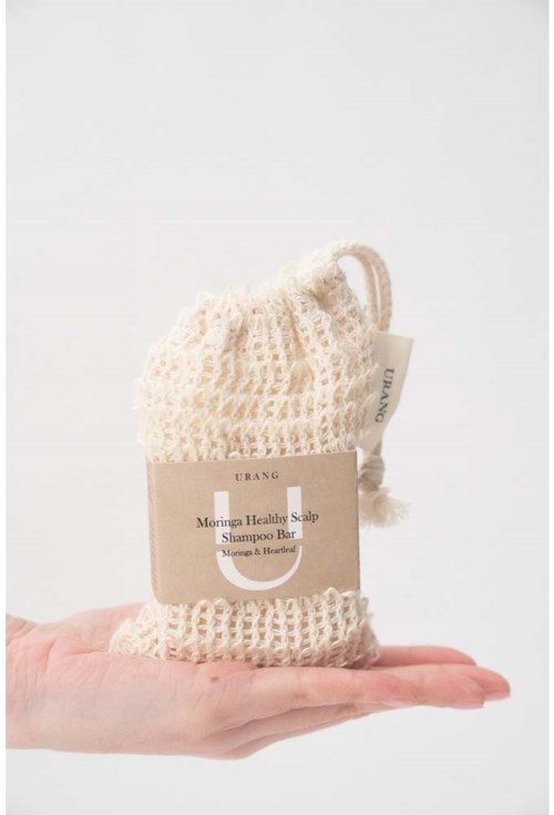 En hånd holder en strikket såpepose med en etikett som sier 'Morina Healthy Scalp Shampoo Bar'.