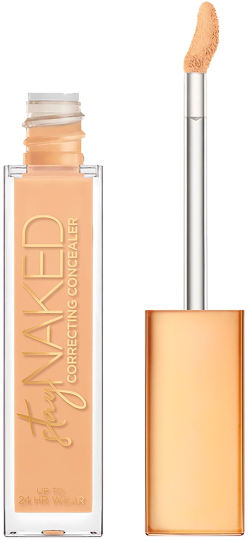 En concealer-flaske med applikator, lys beige produkt og guldhoved. Tekst på flasken siger 'Stay Naked.'